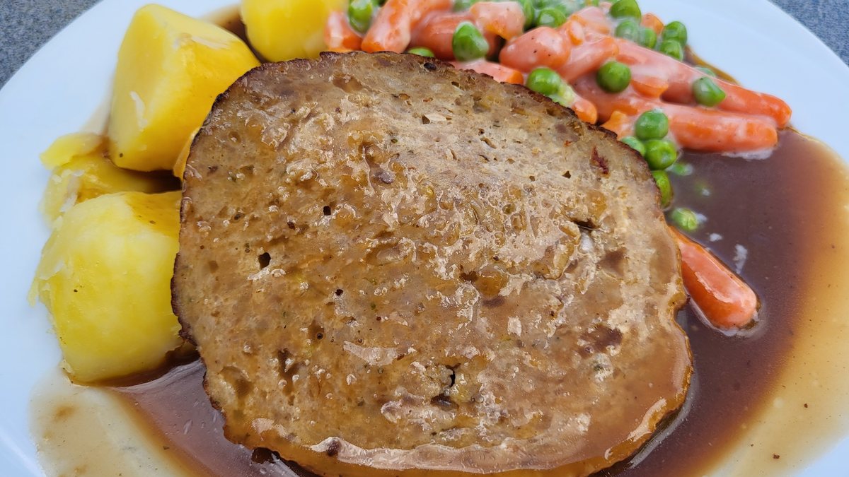 Skive farsbrød med kogte kartofler, brun sovs, ærter og gulerødder på en tallerken