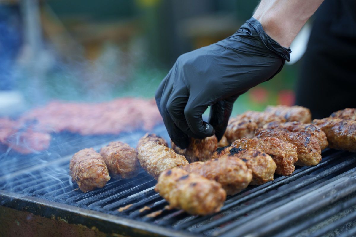 Sorte nitrilhandsker ved vending af pølser på grillen