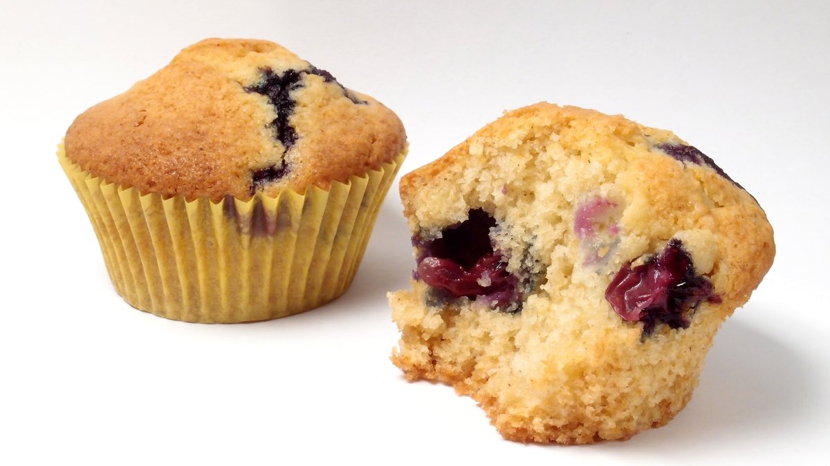 To blåbærmuffins på hvid baggrund, den ene brækket over med synlige blåbær