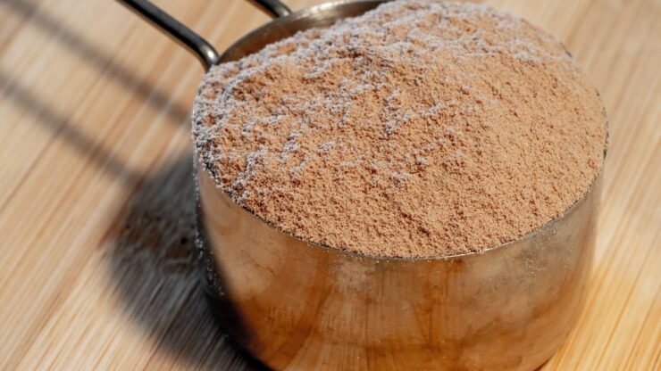 Måleske i metal fyldt med proteinpulver på et bord af bambus
